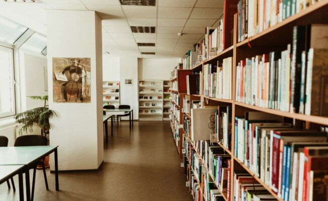 Bibliotēkas telpas, kur labajā pusē ir grāmatas un kreisajā galdi lasīšanai