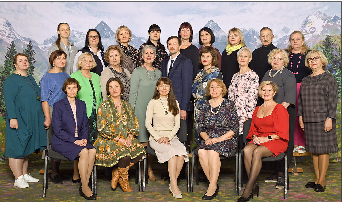 Grupas fotoattēls, kurā redzams Suntažu vidusskolas personāls, galvenokārt sievietes, kas pozē trīs rindās pret kalnu ainavas fonu. Attēla apakšā teksts: Suntažu vidusskola 2022./2023. mācību gads.